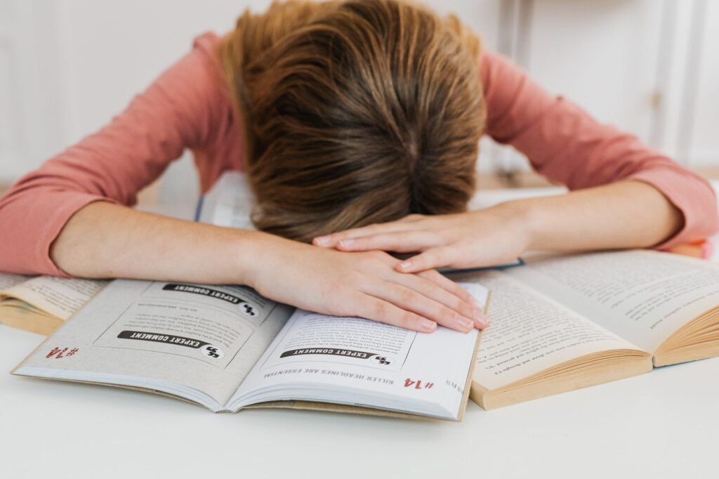 A Student Overwhelmed By Studying Falls Asleep On Open Books At A Desk, Representing Academic Fatigue.