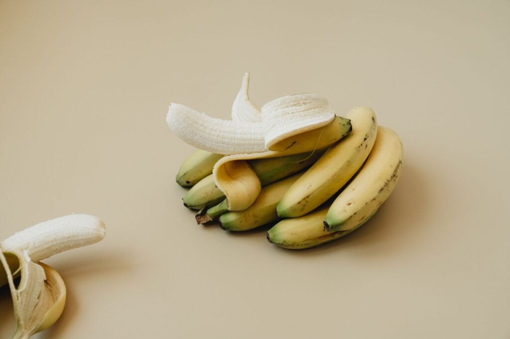 A Bunch Of Ripe Bananas With One Peeled, Displayed On A Neutral Backdrop. Ideal For Food Visuals.