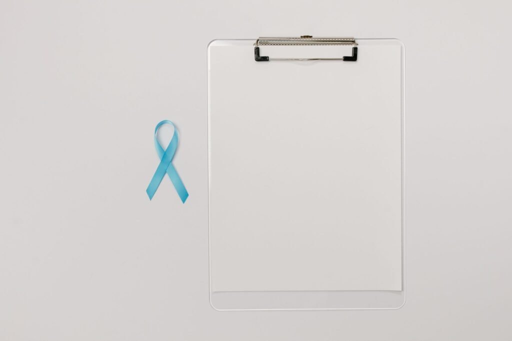 Flat Lay Of A Blue Prostate Cancer Awareness Ribbon And A Clipboard Symbolizing Health Check Ups.