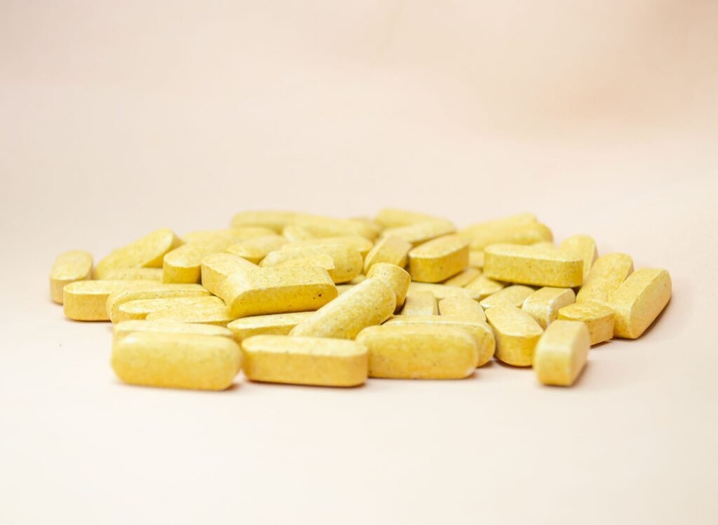 Close Up Of Scattered Yellow Vitamin Tablets On A Light Neutral Background.